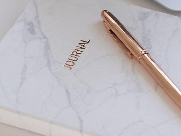 White marble journal with gold lettering and a rose gold pen, perfect for daily journaling and reflection.