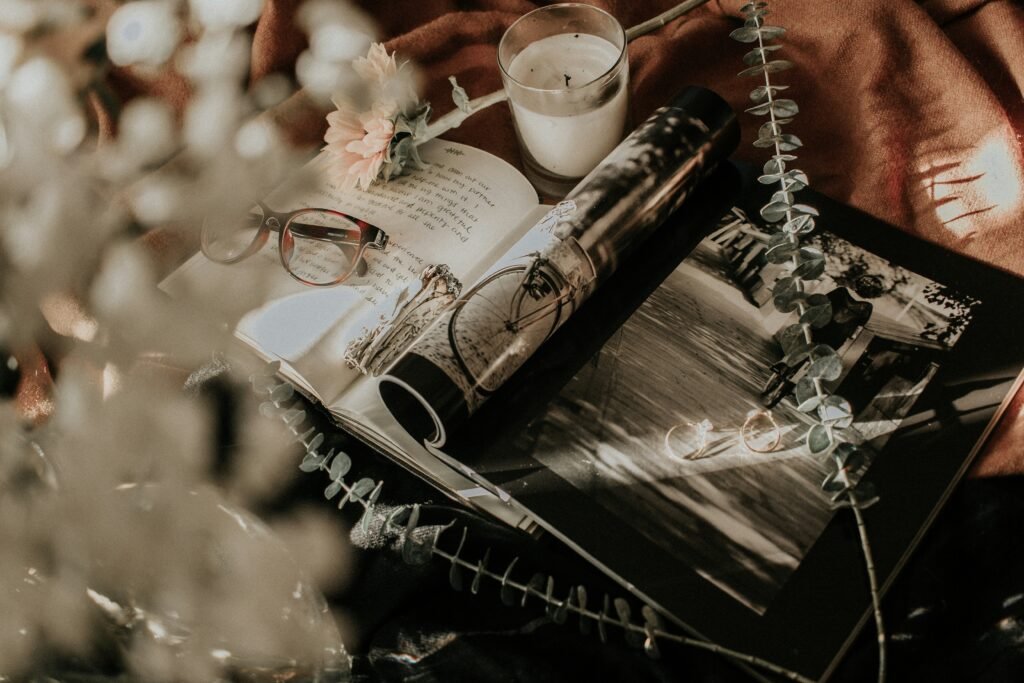  A peaceful flat lay with an open journal filled with reflections, vintage eyeglasses, a calming candle, and a black-and-white photo book, symbolizing clarity, creativity, and the journey to getting unstuck. Eucalyptus leaves and soft lighting evoke a sense of renewal and inspiration.